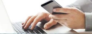 Man Holding Cell Phone and Typing on Computer