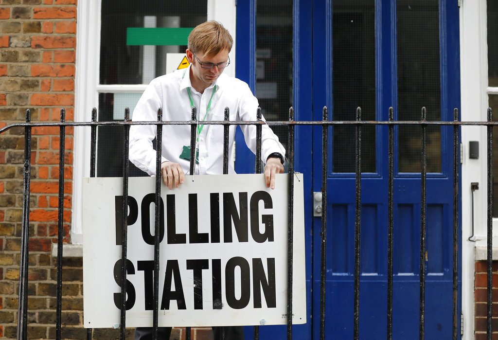 A man fixes a sign to the railings outside a polling station in London ahead of the arrival of Britain's Labour party leader Jeremy Corbyn who will vote in the general election Thursday, June 8, 2017. (AP Photo/Frank Augstein)